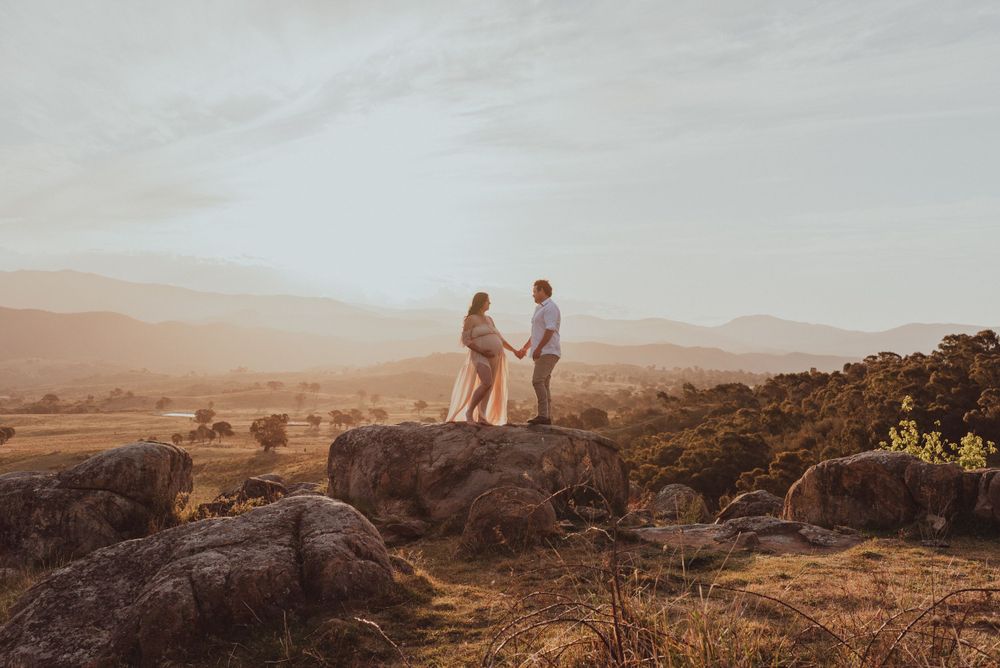 Couple stands on rocky overlook with scenic mountain vista at sunset.