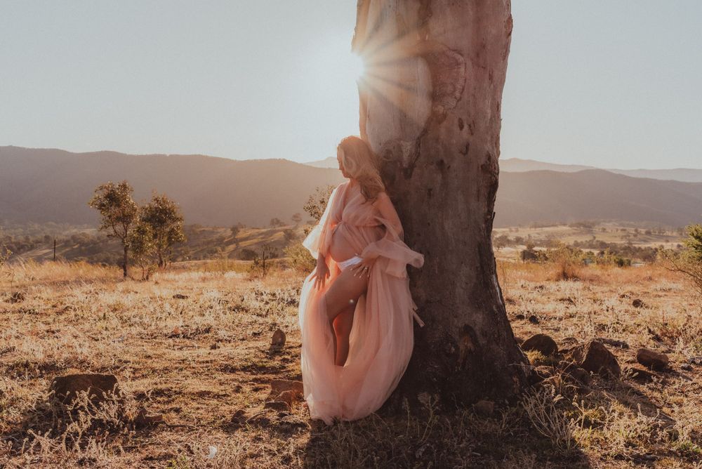 Ethereal portrait against tree trunk during golden hour in rustic landscape.