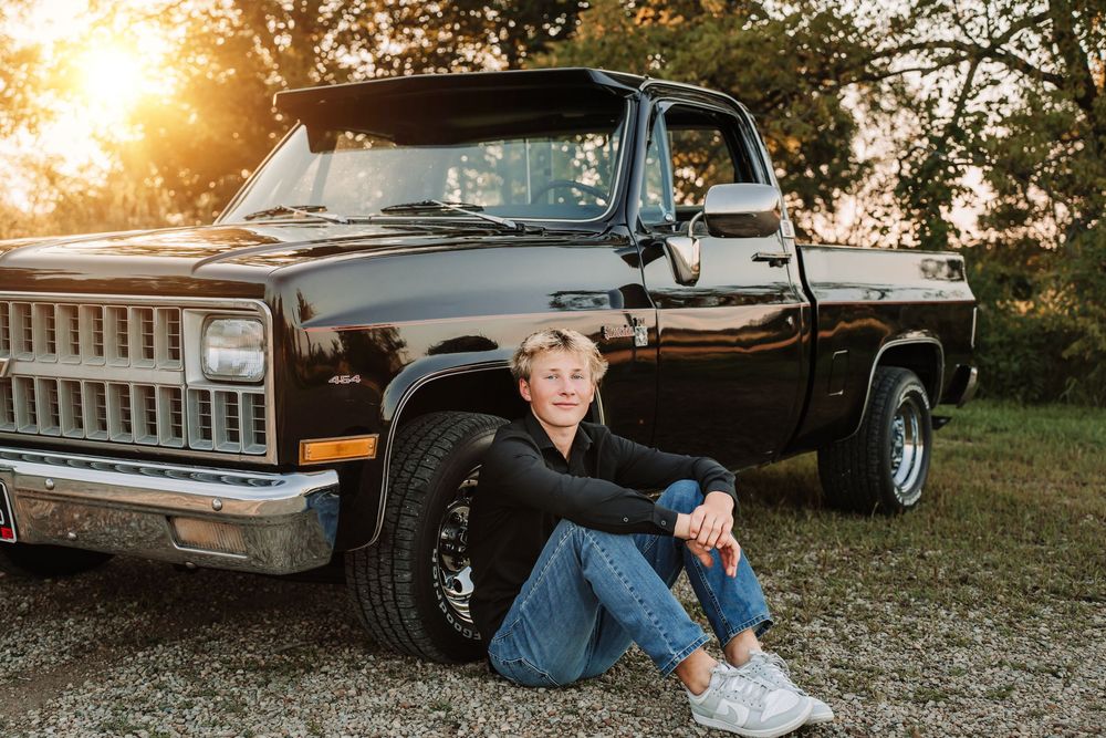 Vintage black Chevrolet pickup truck parked in a grassy field at golden sunset.