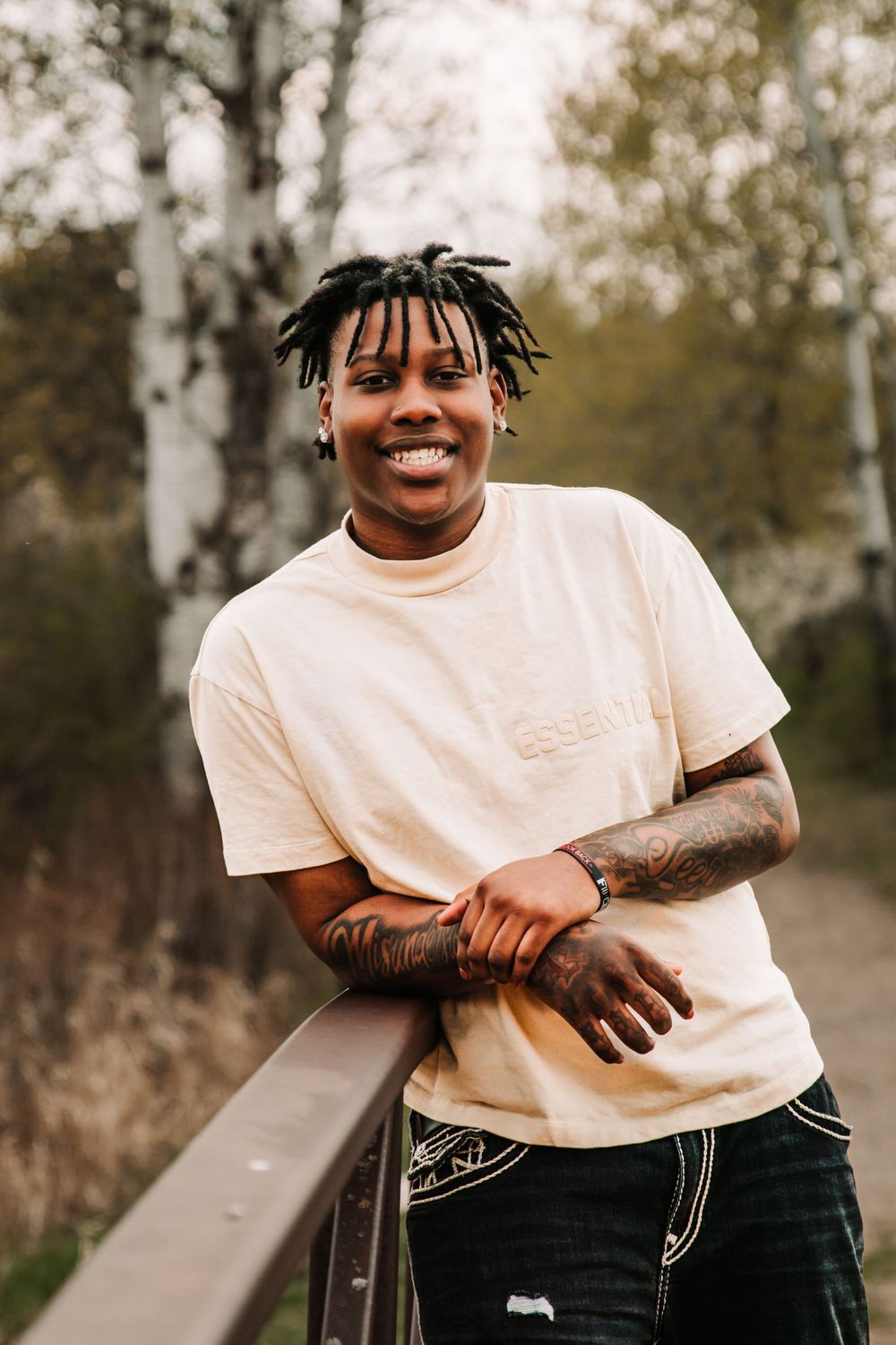 Casual portrait of a person in white t-shirt smiling while leaning on railing outdoors.