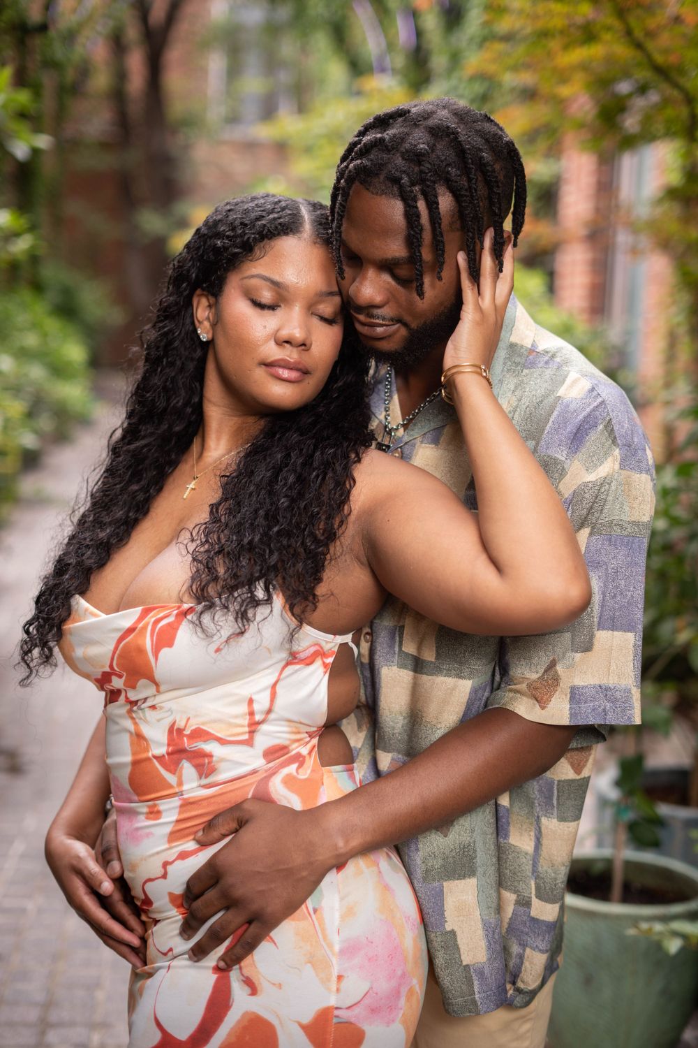 A tender maternity photo of a Black couple embracing on a garden pathway, cradling a baby bump.