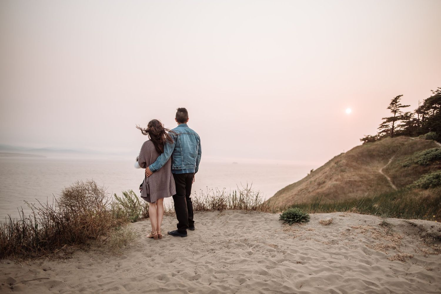 Couple standing together on sandy beach cliff during sunset.