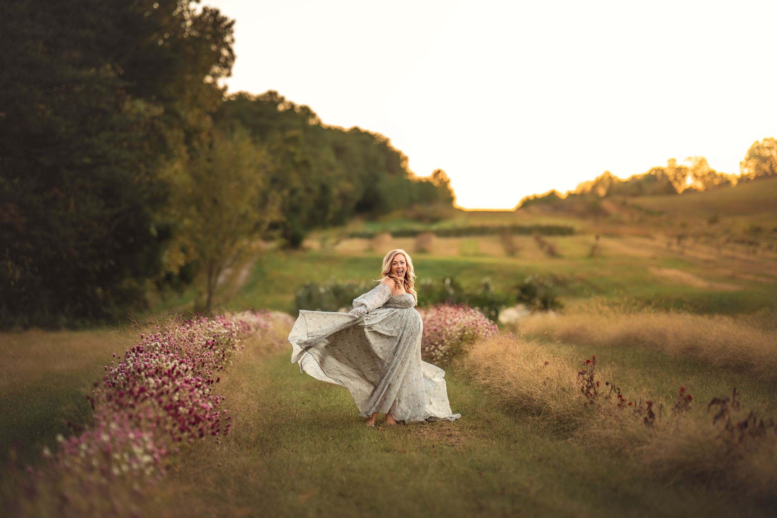 A dreamy sunset scene in a golden meadow with a pregnant woman spinning in a flowing white dress among wildflowers.