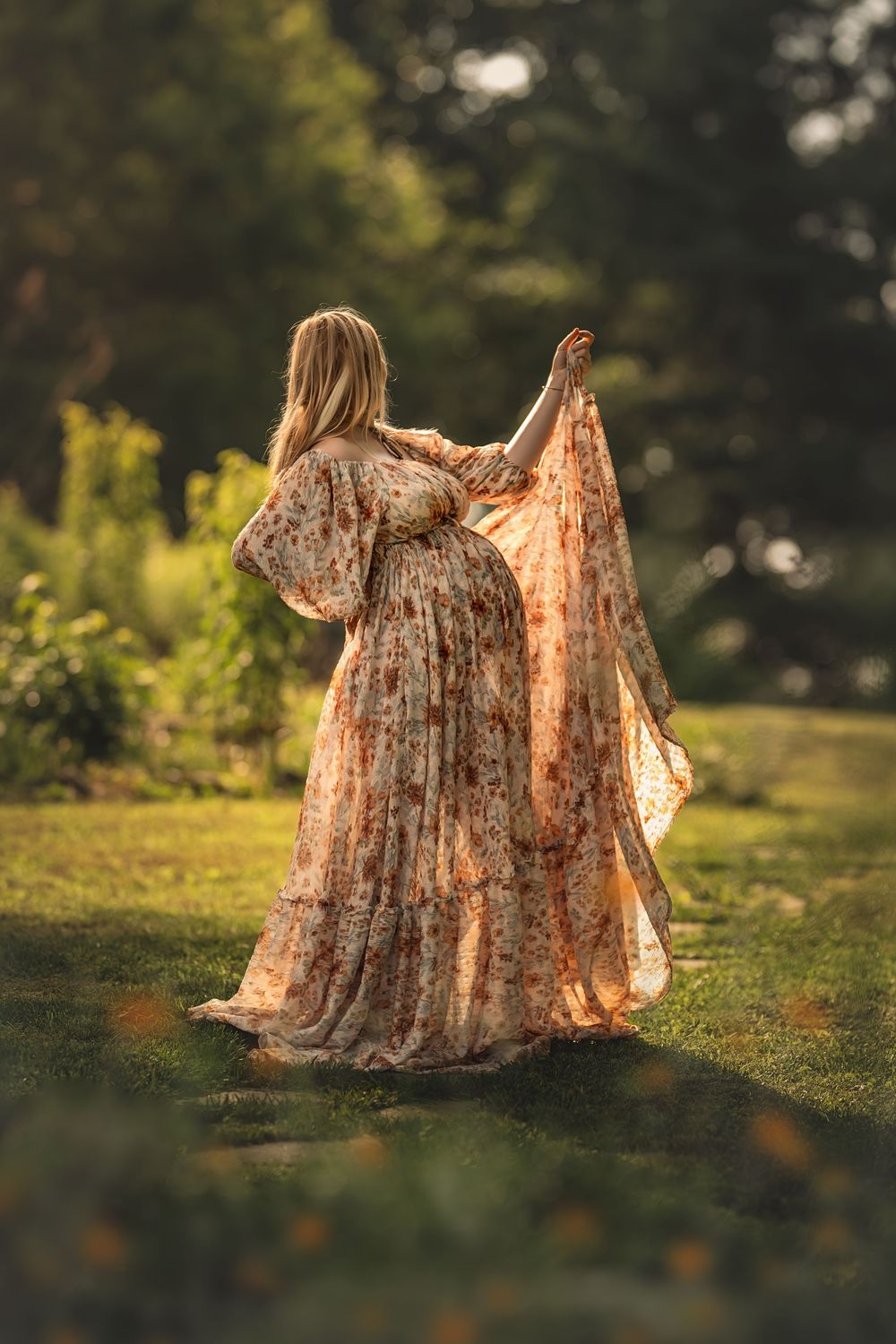 Romantic garden scene capturing a flowing dress and golden sunlight silhouette of a pregnant woman through a blooming summer meadow.