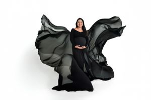Pregnant woman in black dress with billowing fabric against white background for studio maternity session.