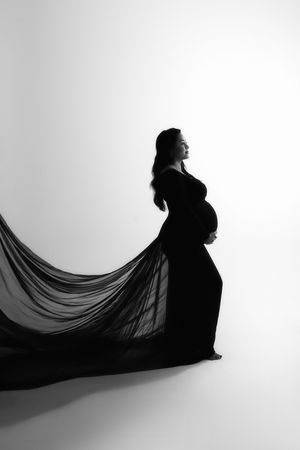 A dramatic black and white photo series showing a pregnant silhouette with flowing dark fabric creating dynamic movement against white.