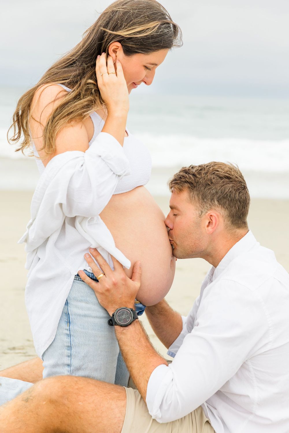 A tender maternity moment captured on the beach as an expecting couple shares an intimate moment by the ocean.