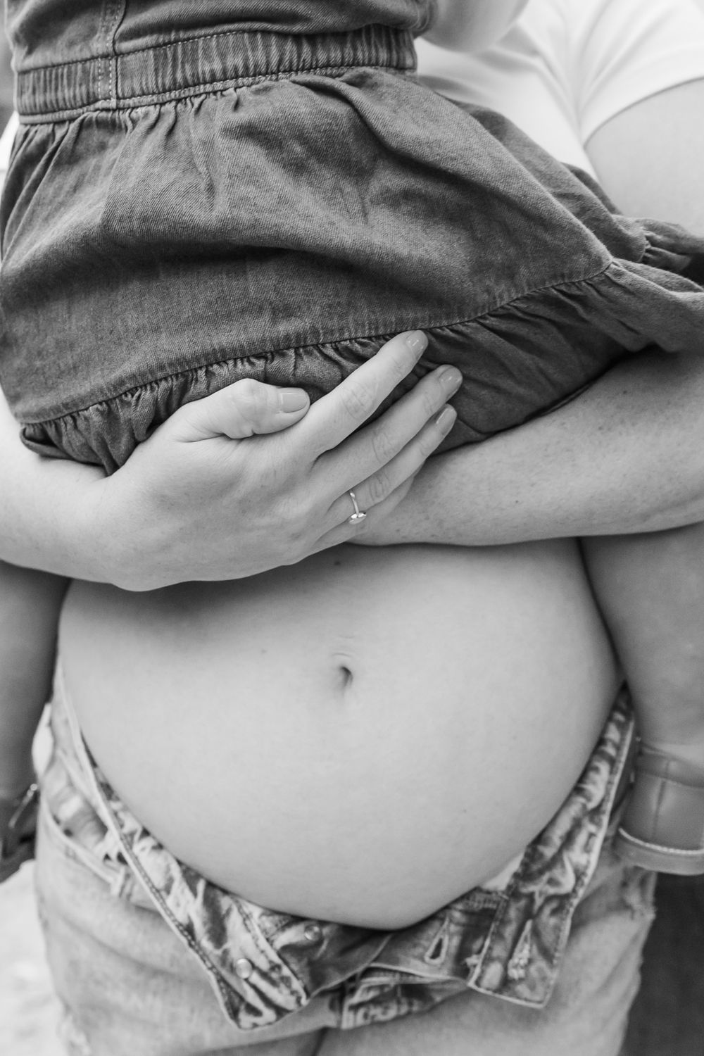 Black and white close-up of a pregnant belly with camo print shorts pulled down to show the bare abdomen.