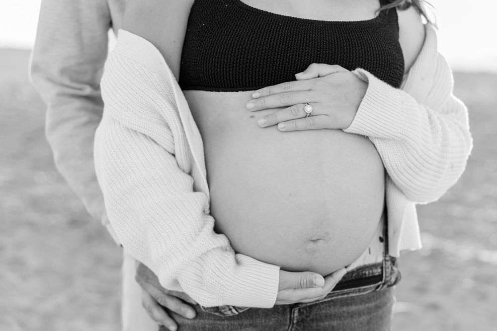 Black and white photo of pregnant belly being cradled by hands in a cozy white sweater. carlsbad maternity photographer