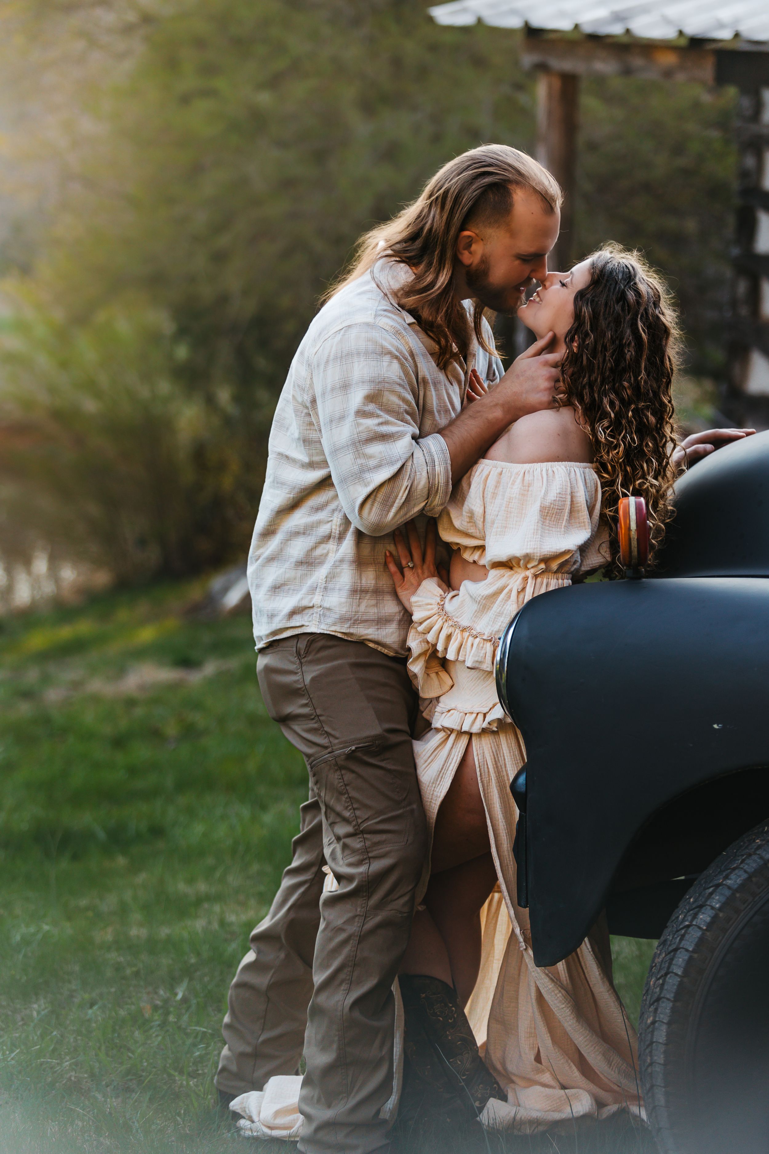 A romantic moment shared between a couple against a vintage car at sunset.