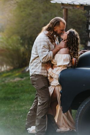 A romantic moment shared between a couple against a vintage car at sunset.