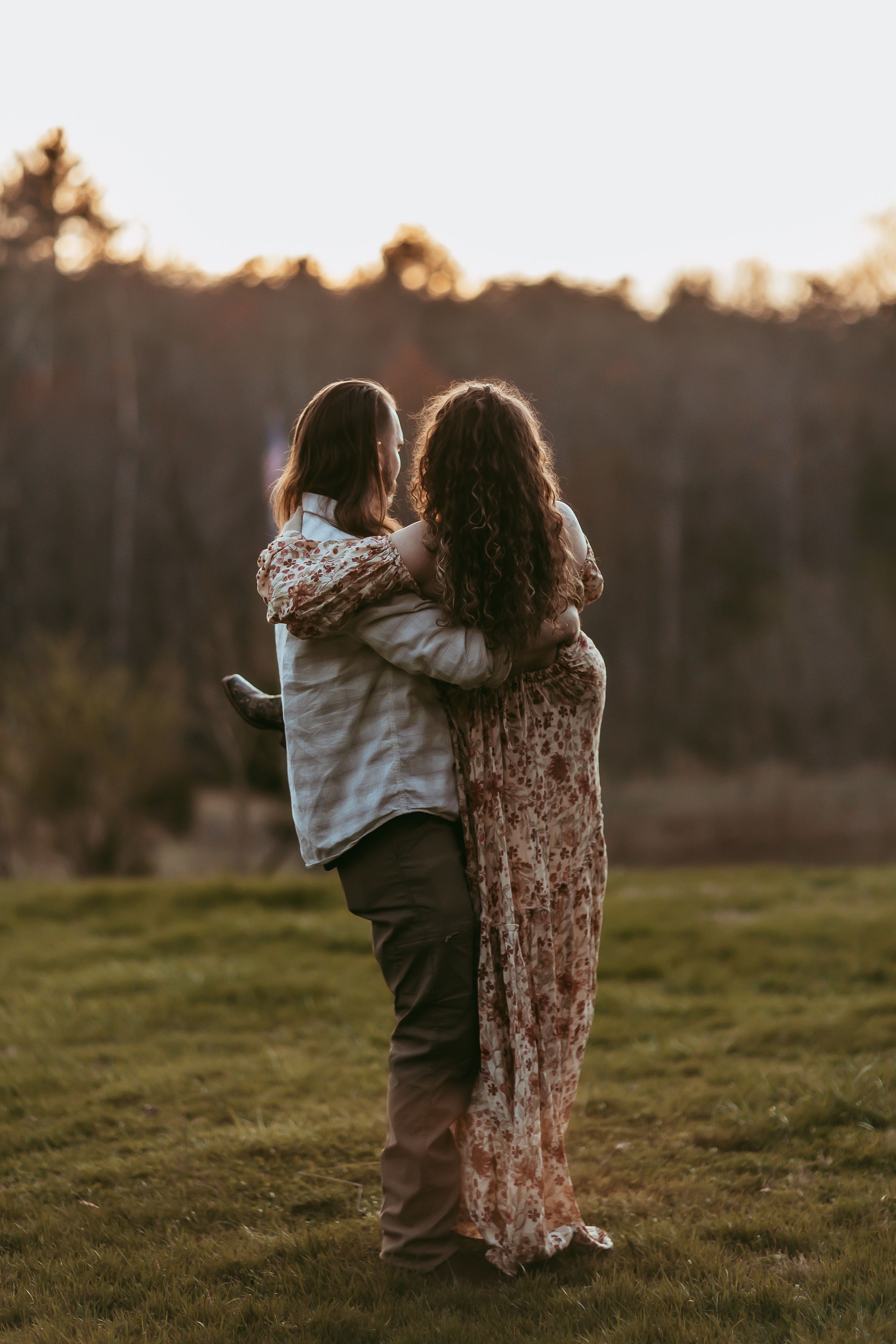 Two people embrace while standing in a golden-lit field at dusk.