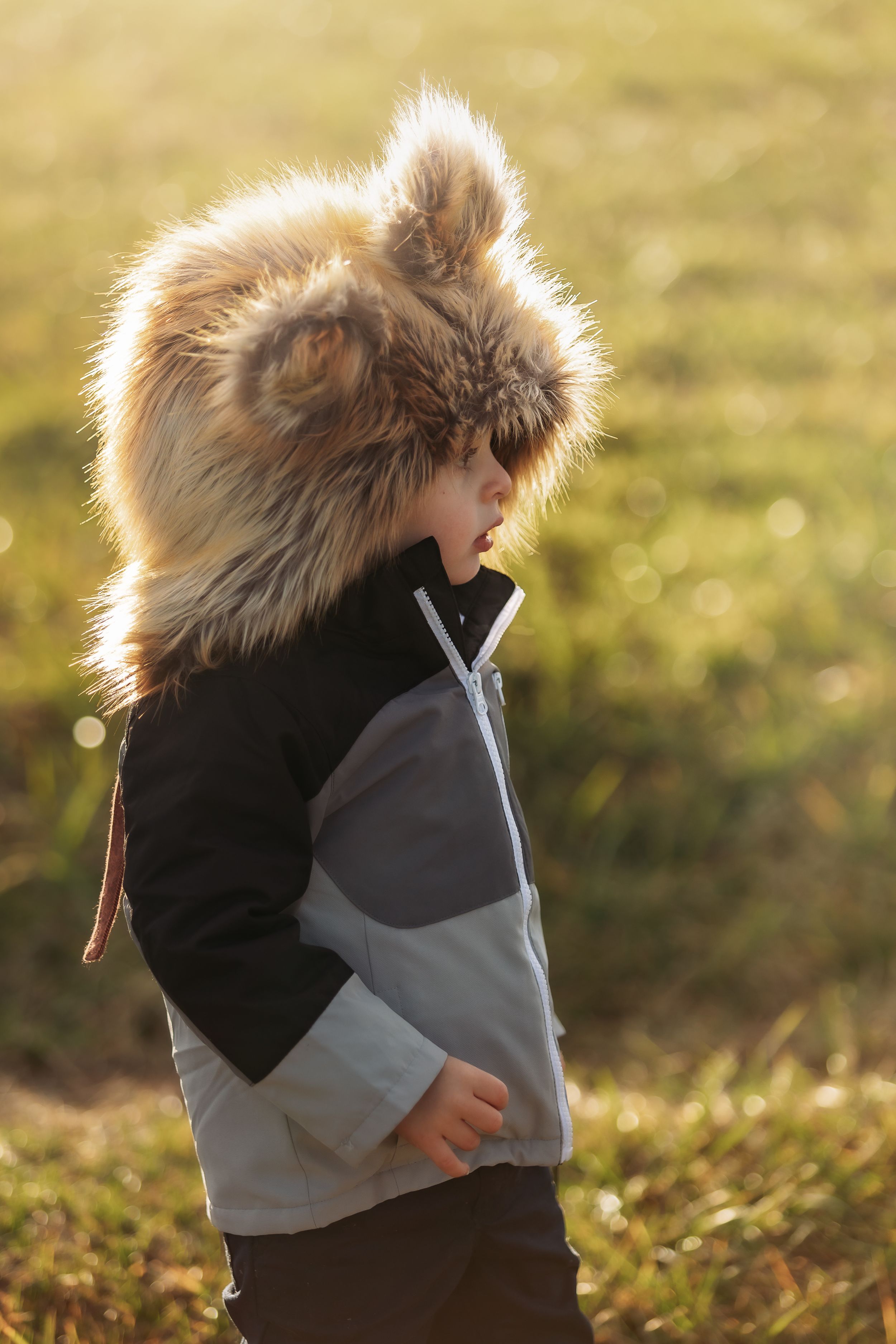 Child in furry hooded coat backlit by golden sunset glow.