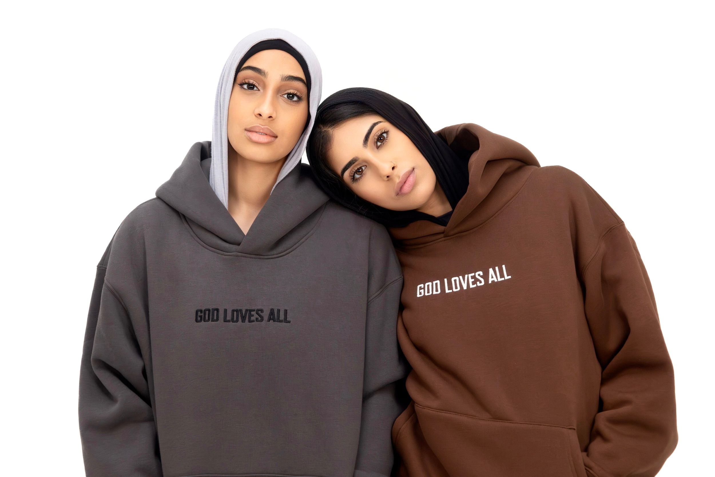 Two people wearing matching 'God Loves All' hoodies in gray and brown colors pose together in a casual photo.