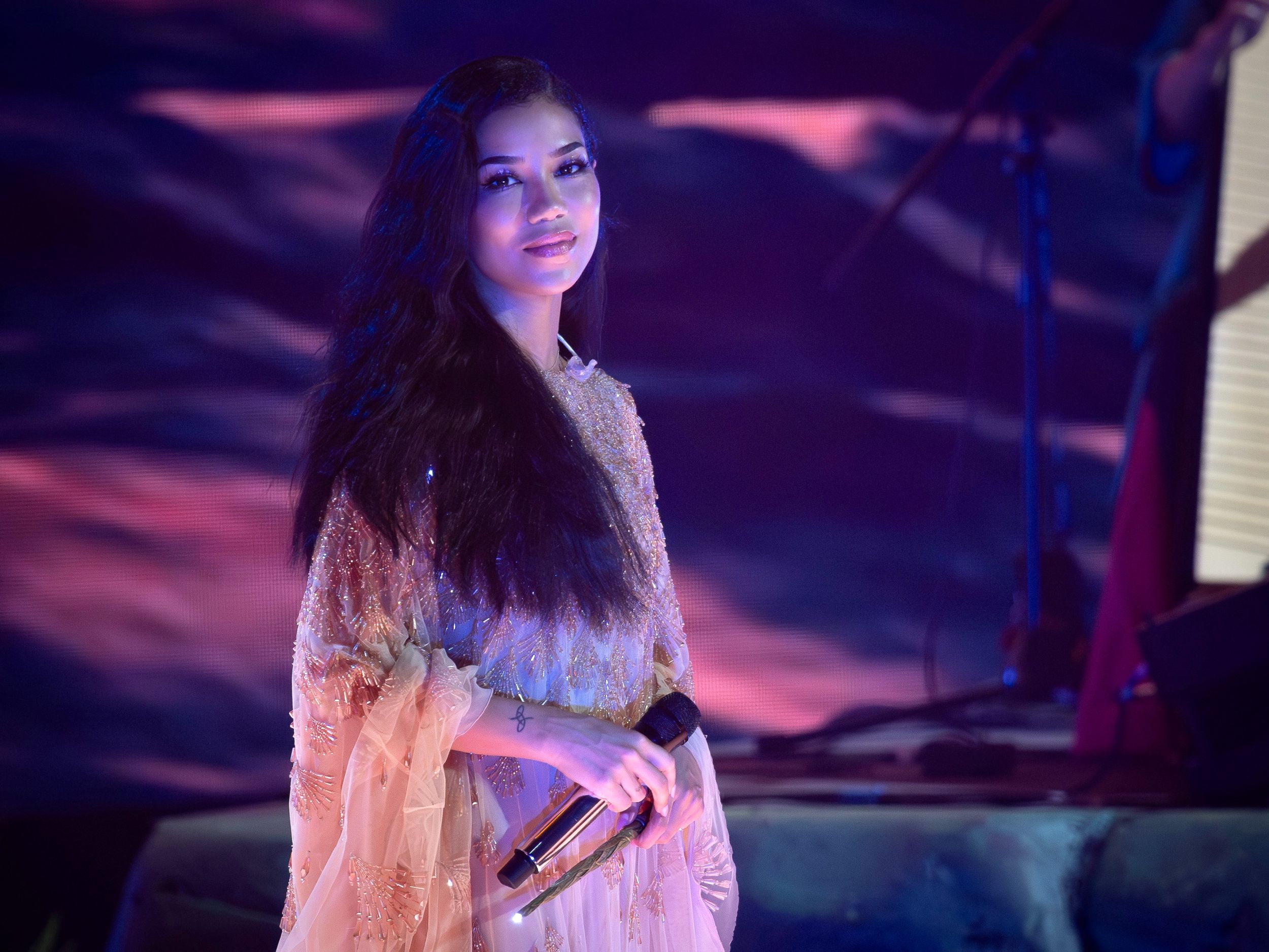 Singer performing on stage in white dress with dramatic purple lighting effects.