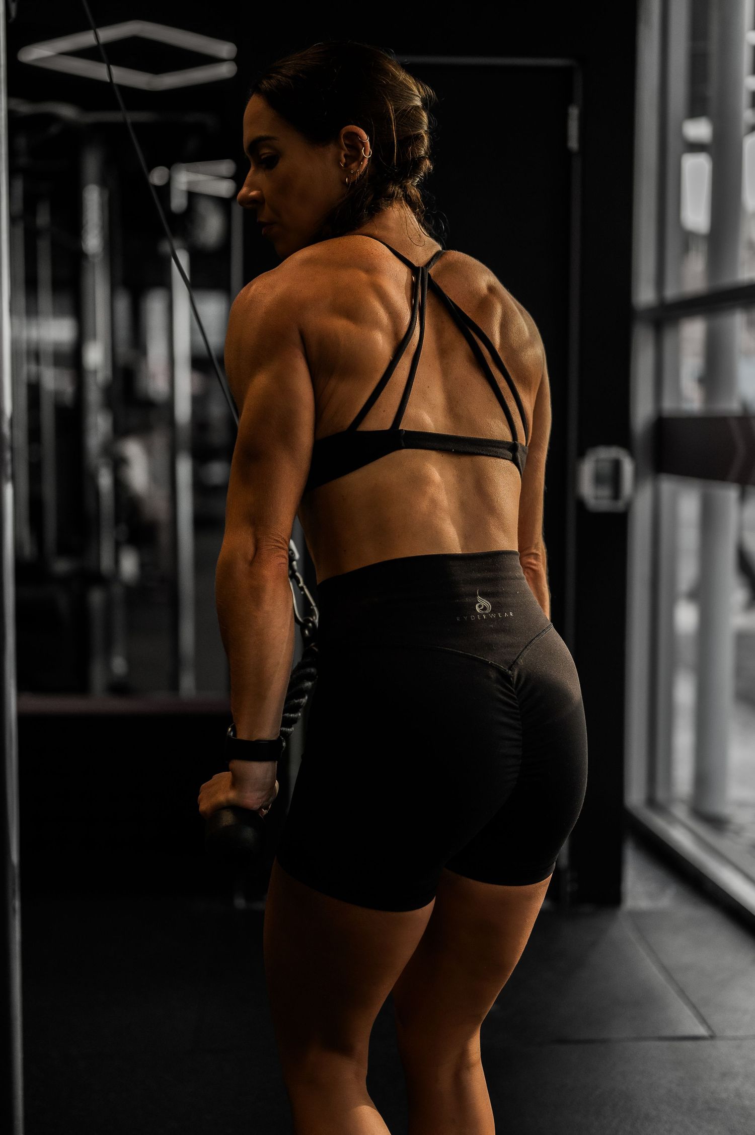 Athletic person wearing black workout shorts and sports bra performs exercises in a dimly lit gym setting.
