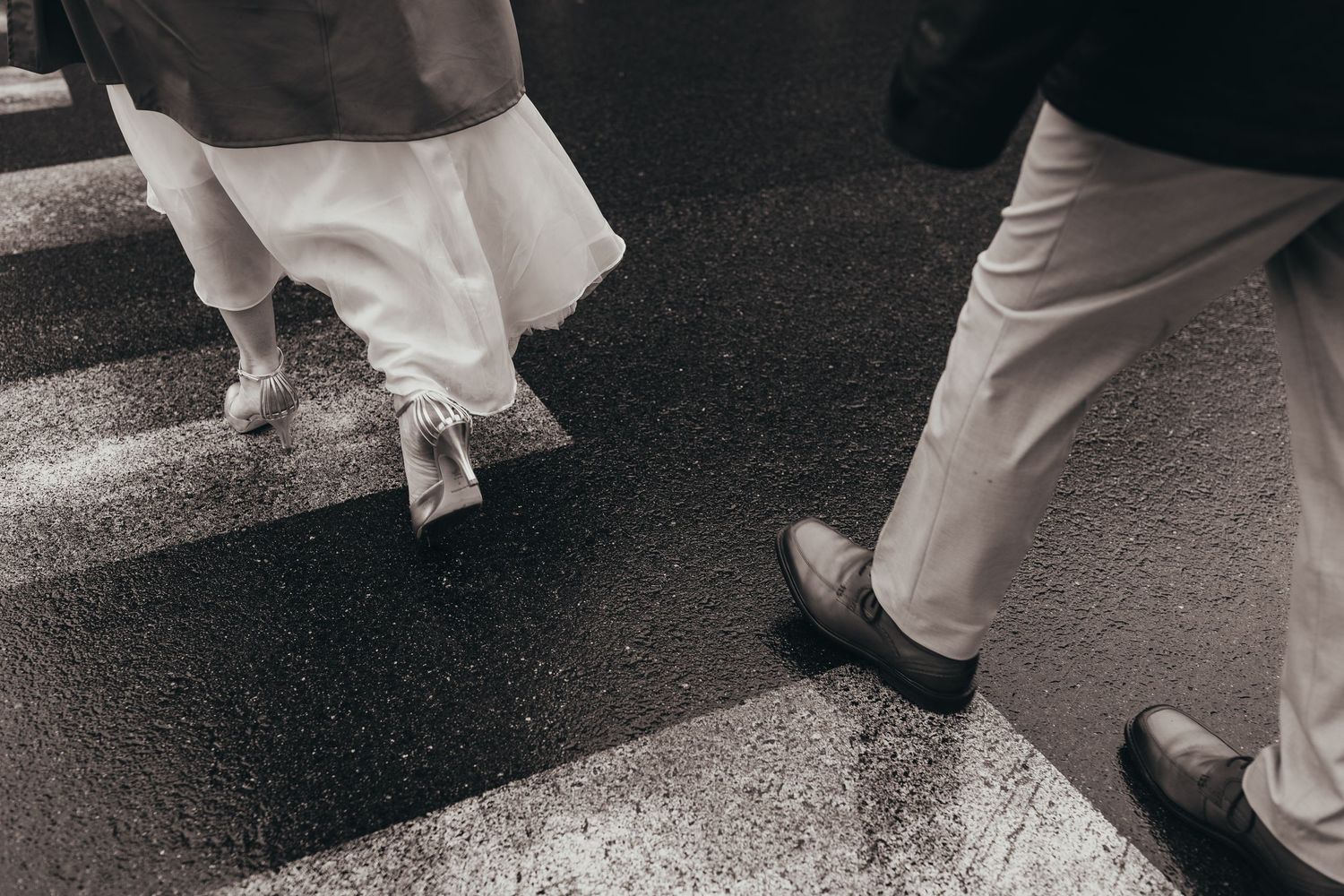 Artistic black and white photo of feet walking on pavement with flowing white dress fabric.