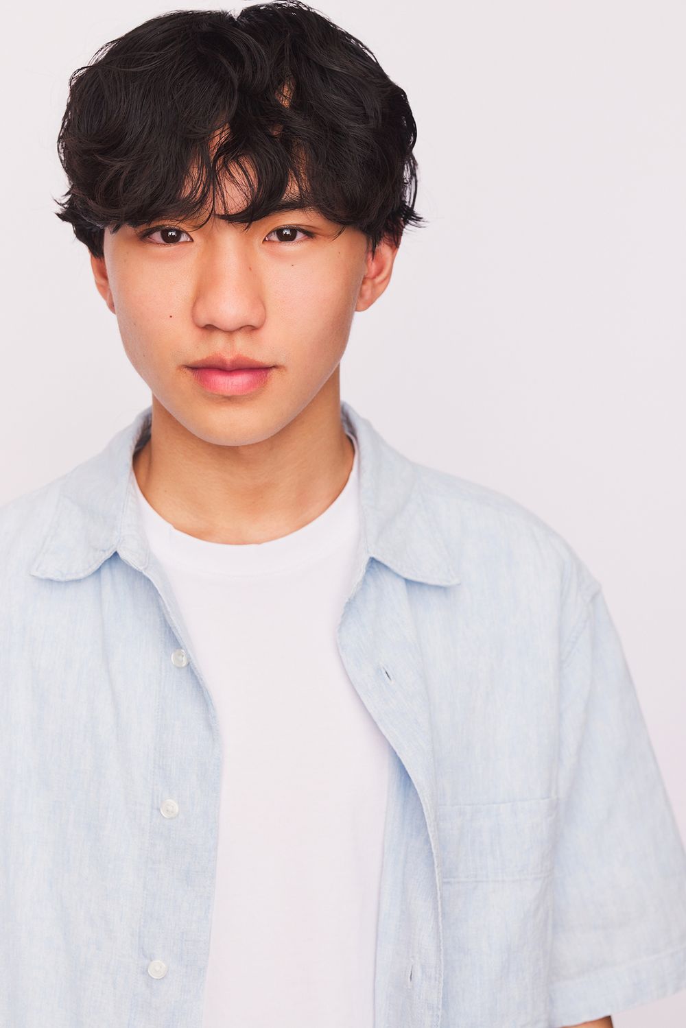 Teen actor Ian Chen wearing a light blue button-up shirt and white t-shirt poses against a white background.