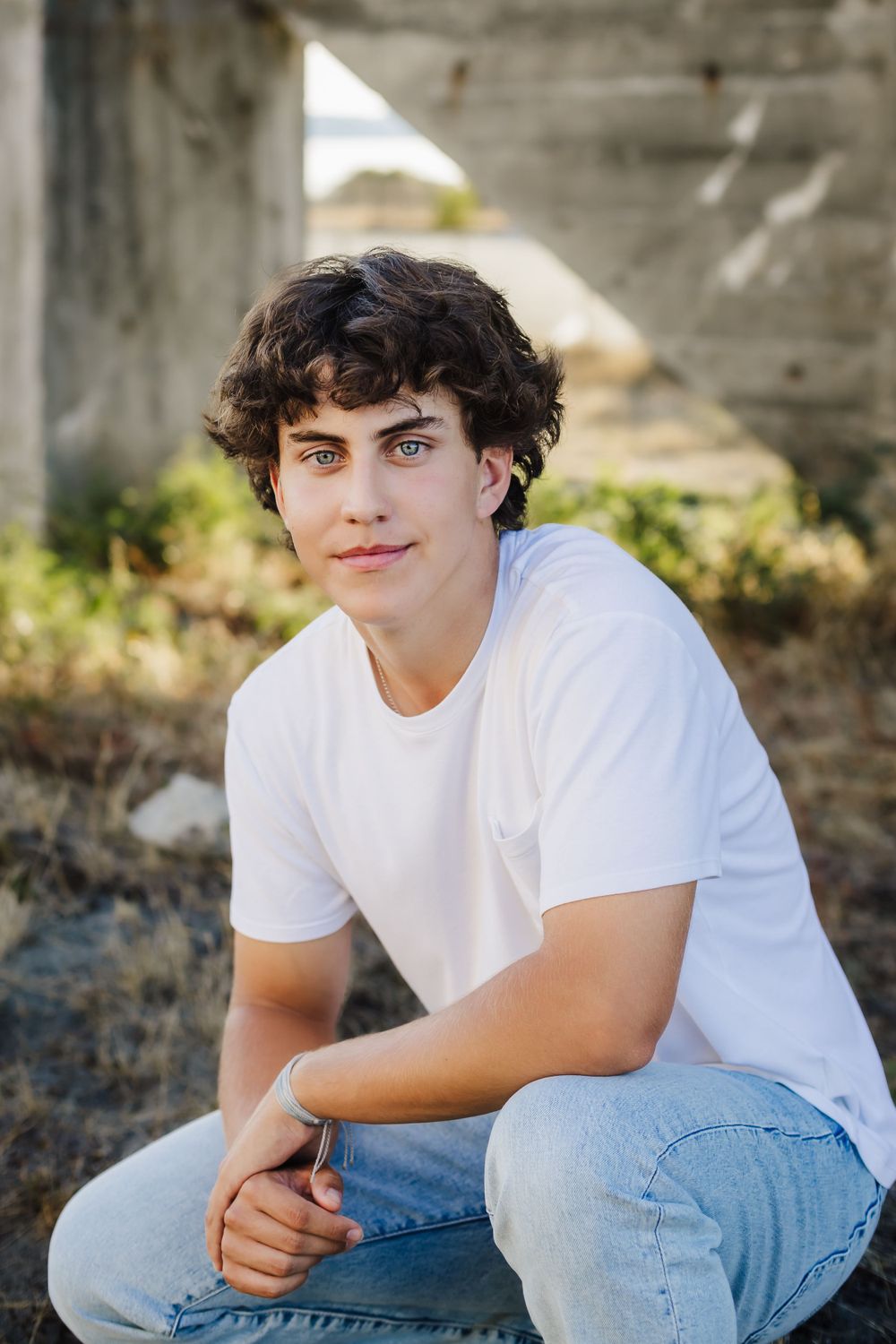 A casual portrait against concrete featuring a white t-shirt and jeans in natural light.