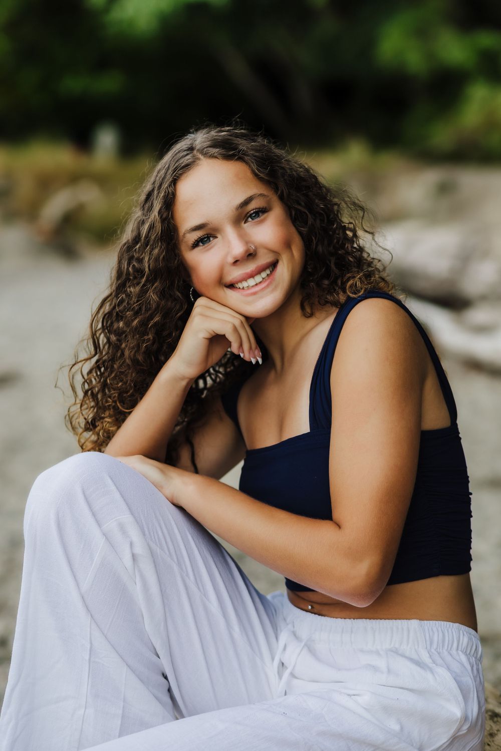 Outdoor portrait in a navy crop top and white pants with natural curly hair.