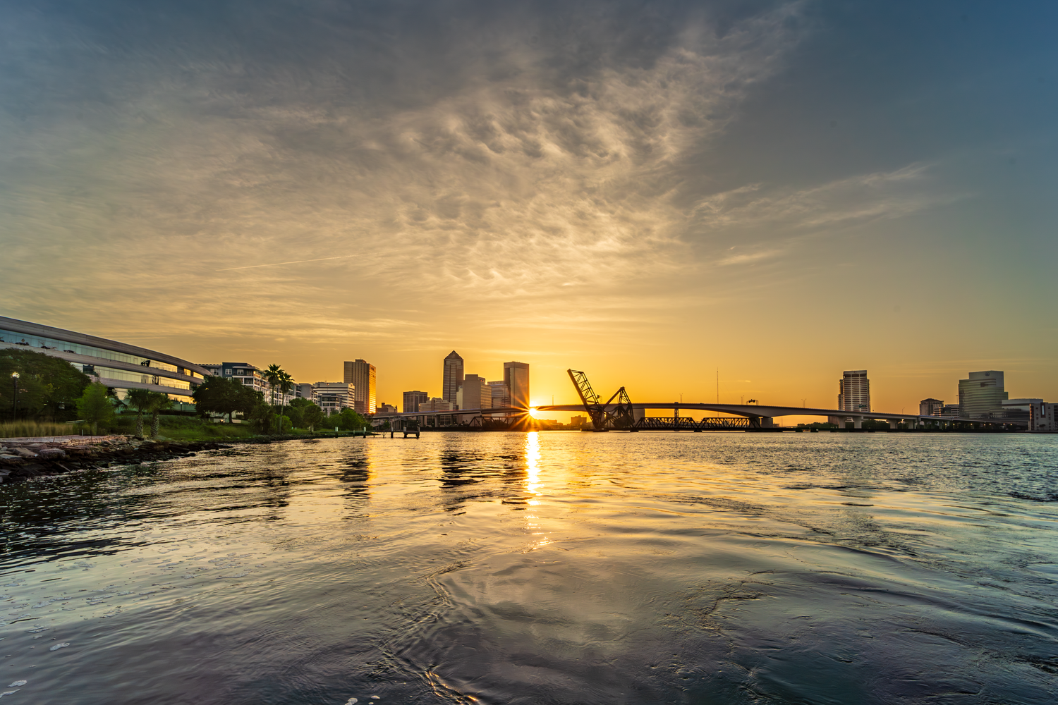 Dramatic sunrise with silhouettes of Jacksonville FL downtown skyline along St. Johns River with golden reflections on water May 30, 2025