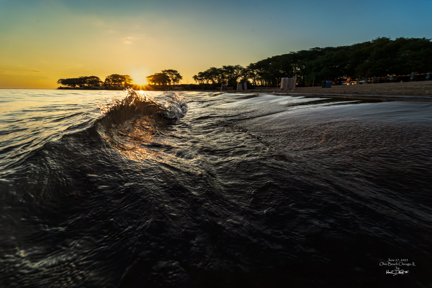 A dramatic sunrise photo shows waves crashing against a reflective shore with golden skies above. Taken in Chicago IL on June 27, 2025