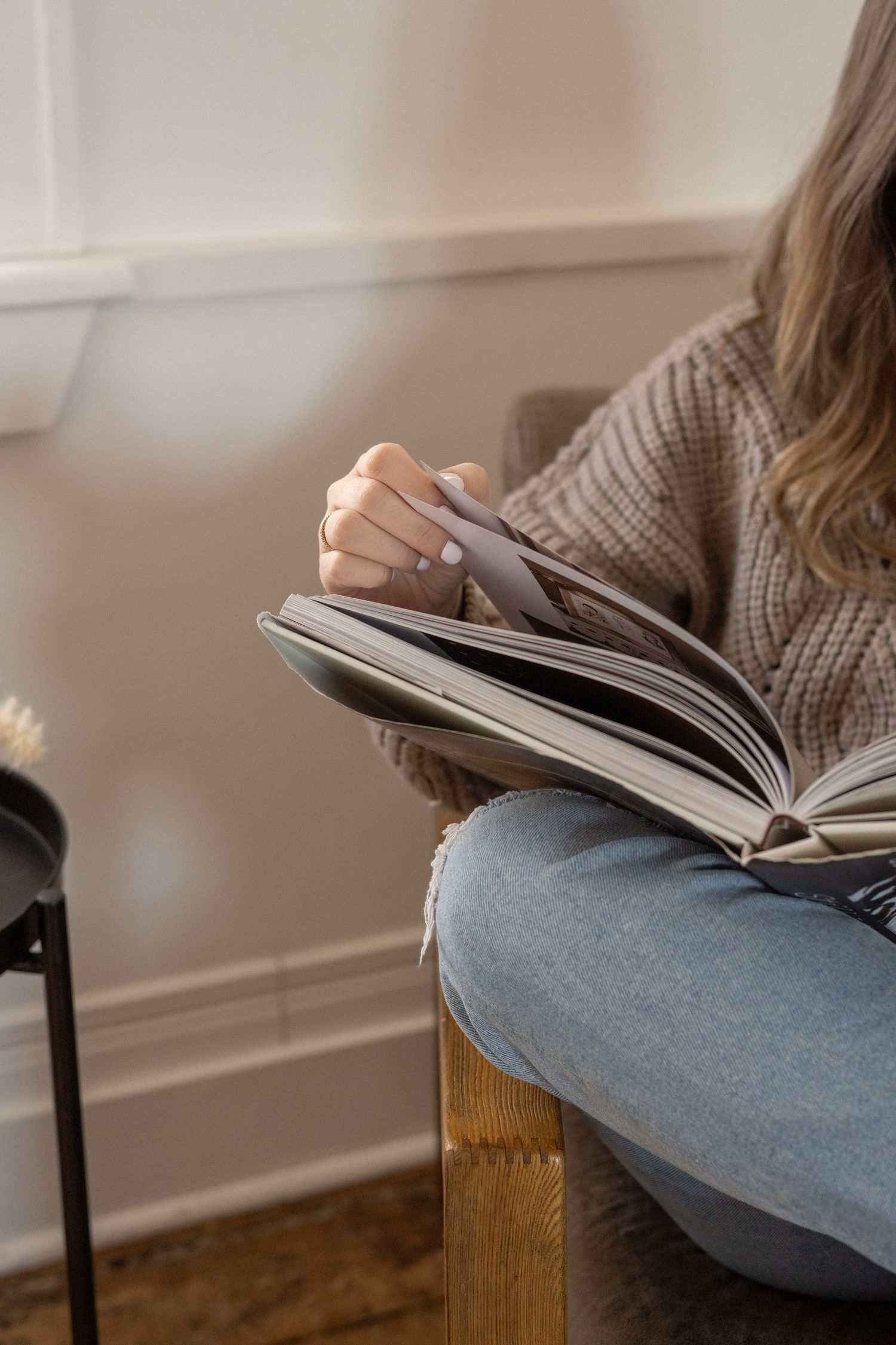 Person in gray sweater and jeans reading a book while sitting in a cozy corner.