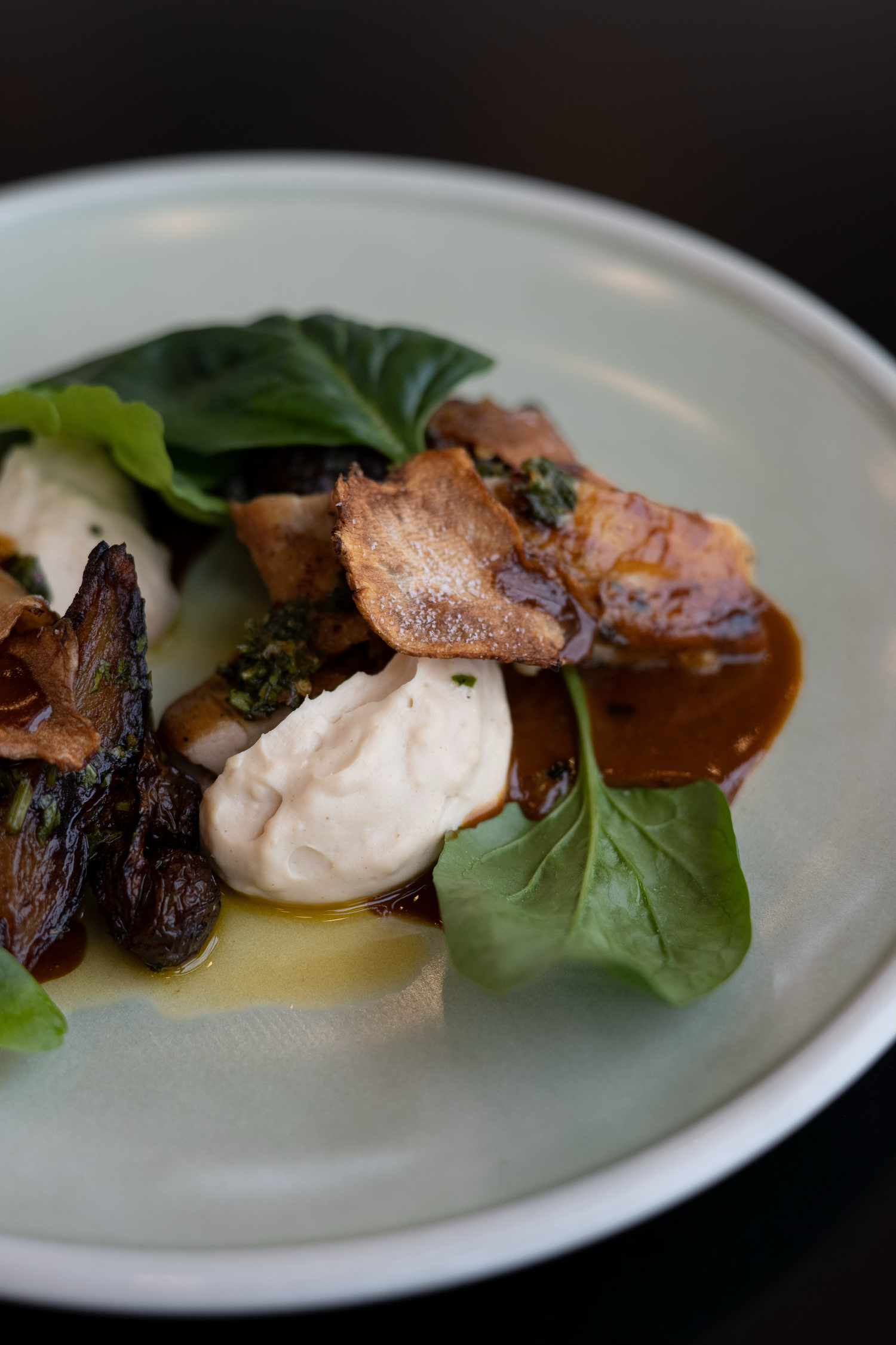 Elegant plated dish featuring meat, greens and sauce on white ceramic plate.