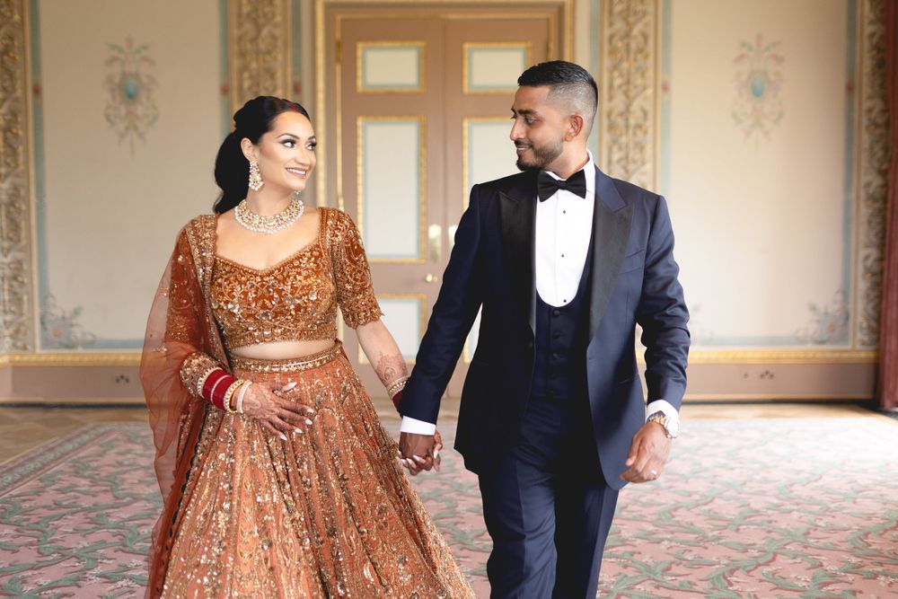 A couple walks hand in hand through an ornate ballroom wearing formal wedding attire. Asian Wedding Photography & Videography