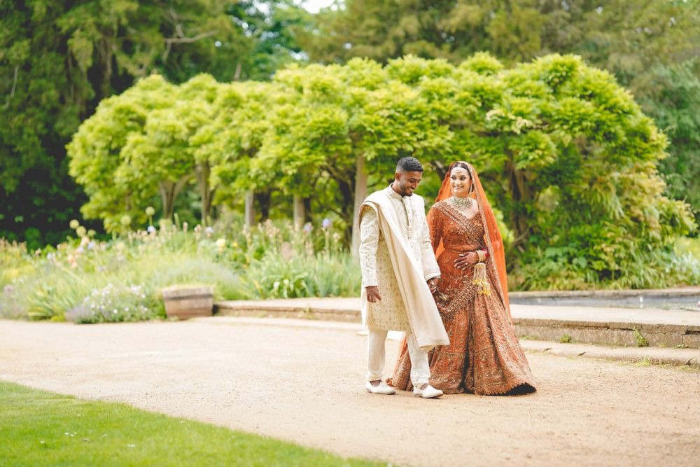 Newlyweds in traditional Indian wedding attire walking through a garden path. Asian Wedding Photography & Videography