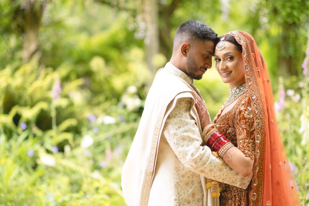 Tender moment between newlyweds in traditional Indian wedding outfits amid garden greenery. Asian Wedding Photography & Videography