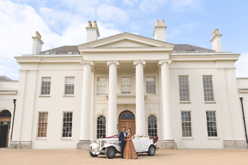 A vintage white car parked in front of a grand Georgian-style mansion with white columns and symmetrical windows. Asian Wedding Photography