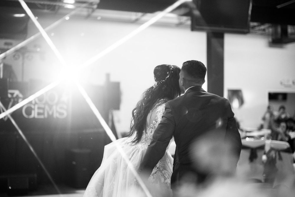 A romantic black and white shot of a couple dancing at their wedding reception with dramatic backlighting creating lens flare.