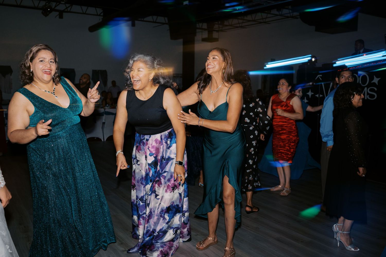Party guests dancing together on a dimly lit dance floor with blue lighting overhead.
