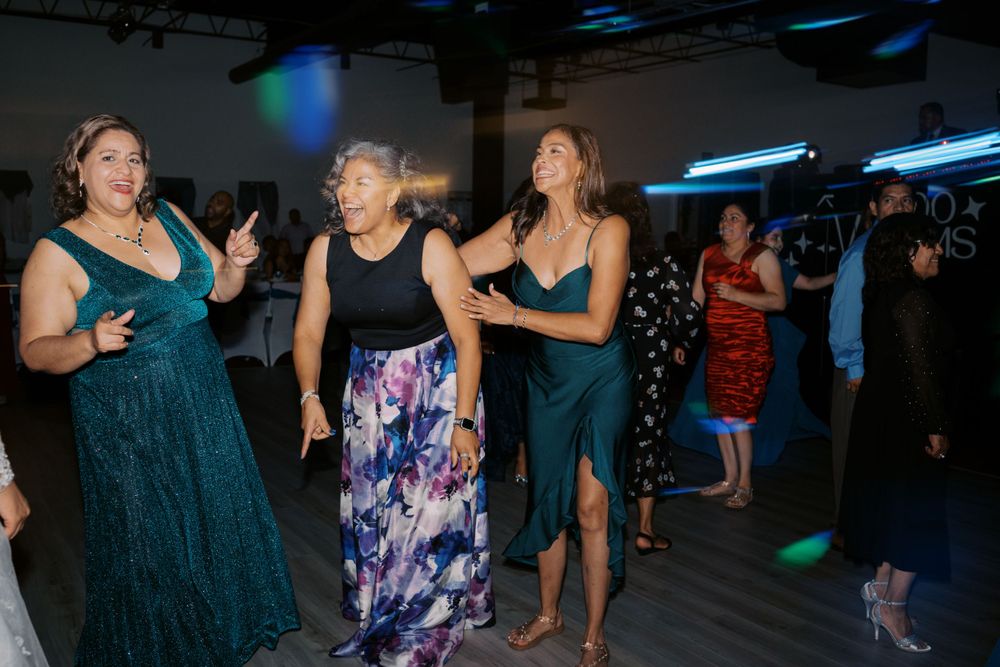 Party guests dancing together on a dimly lit dance floor with blue lighting overhead.