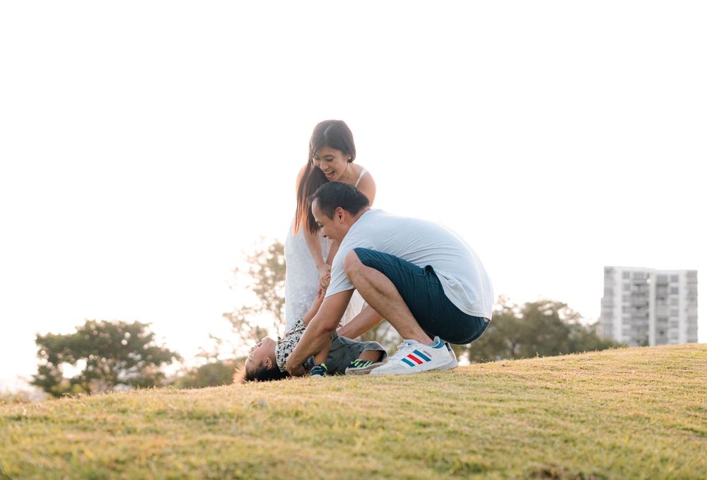 A couple sits together on a grassy hillside during golden hour at sunset.