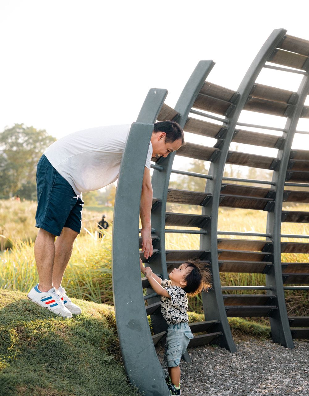 Parent and child interact playfully on a curved climbing structure in a park.