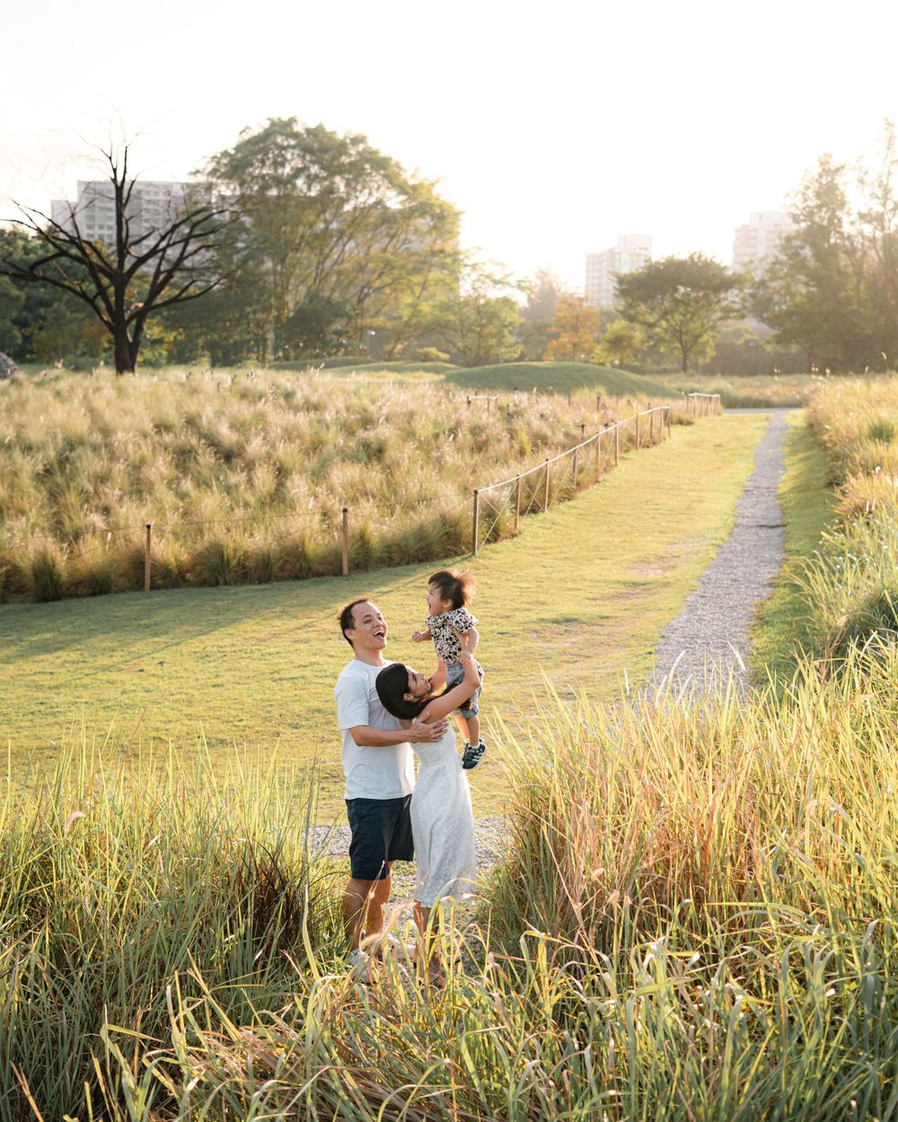 A family embraces in a scenic field with tall grass and a walking path at sunset.