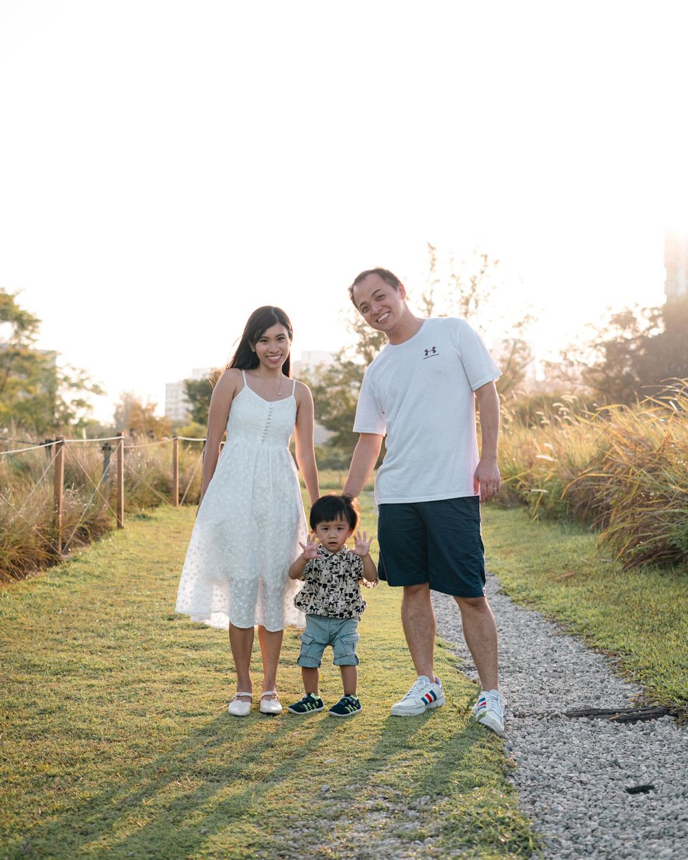 Family enjoying a sunset walk together on a gravel path surrounded by tall grass and natural scenery.