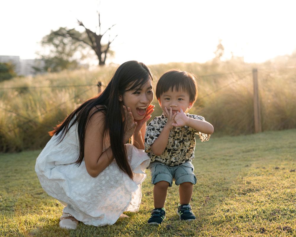 Candid moment of mother and toddler sharing a laugh outdoors during golden hour.