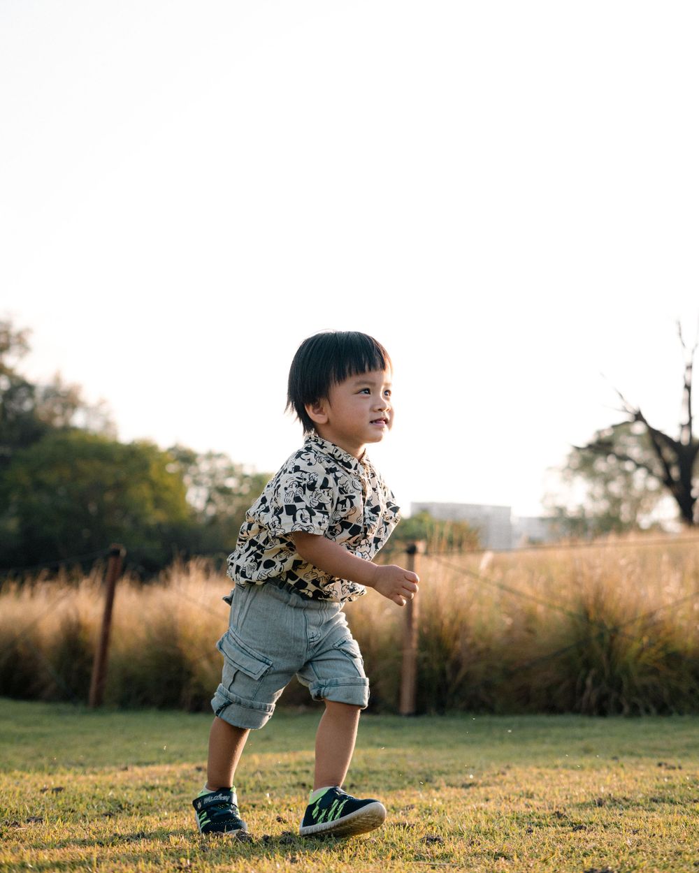 A child in patterned shirt and denim shorts plays on a grassy field at sunset.