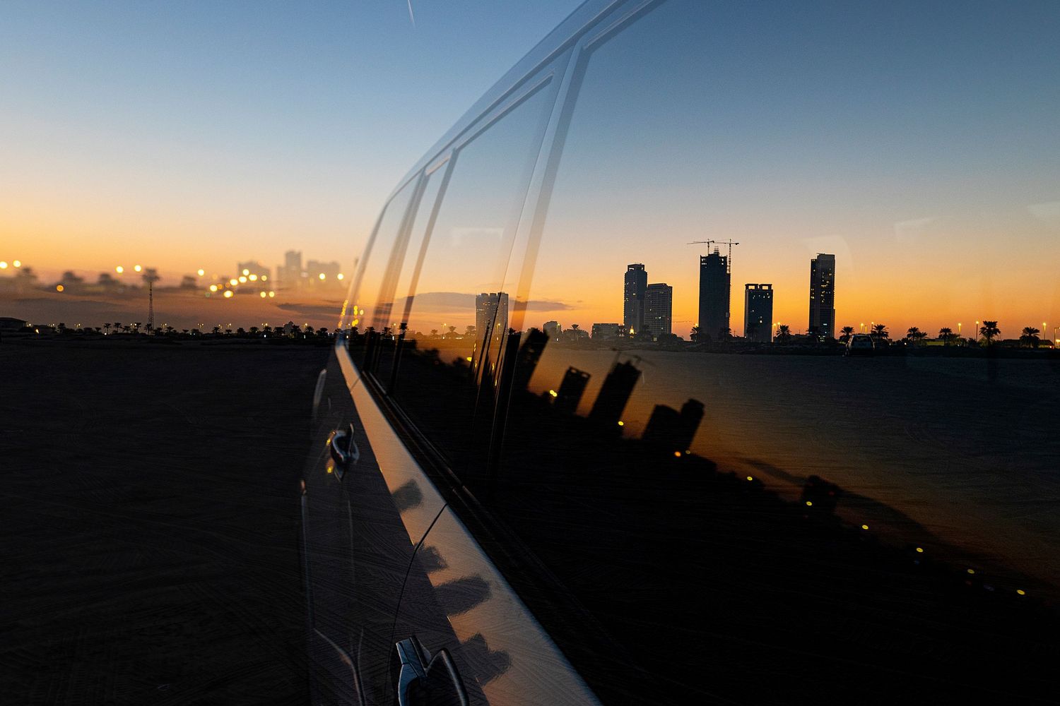 City skyline silhouetted against an orange sunset sky with a curved railing in the foreground.