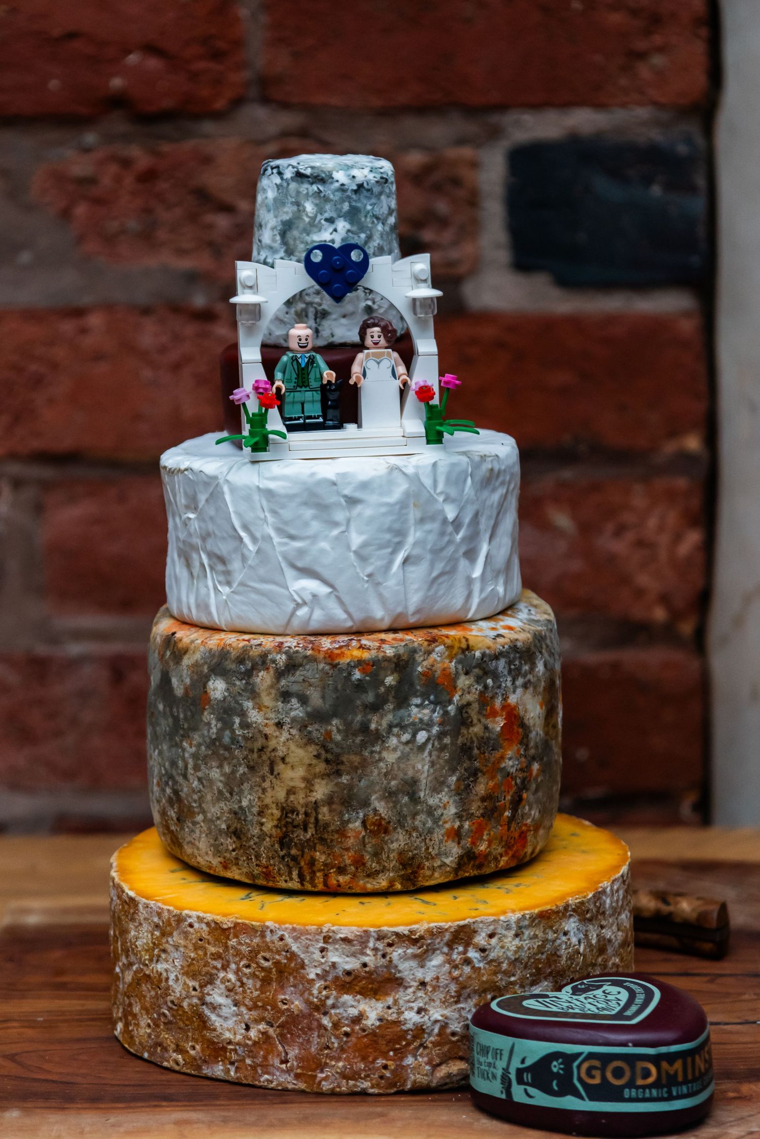 Three-tiered rustic cheese wheel wedding cake decorated with miniature figurines and flowers.