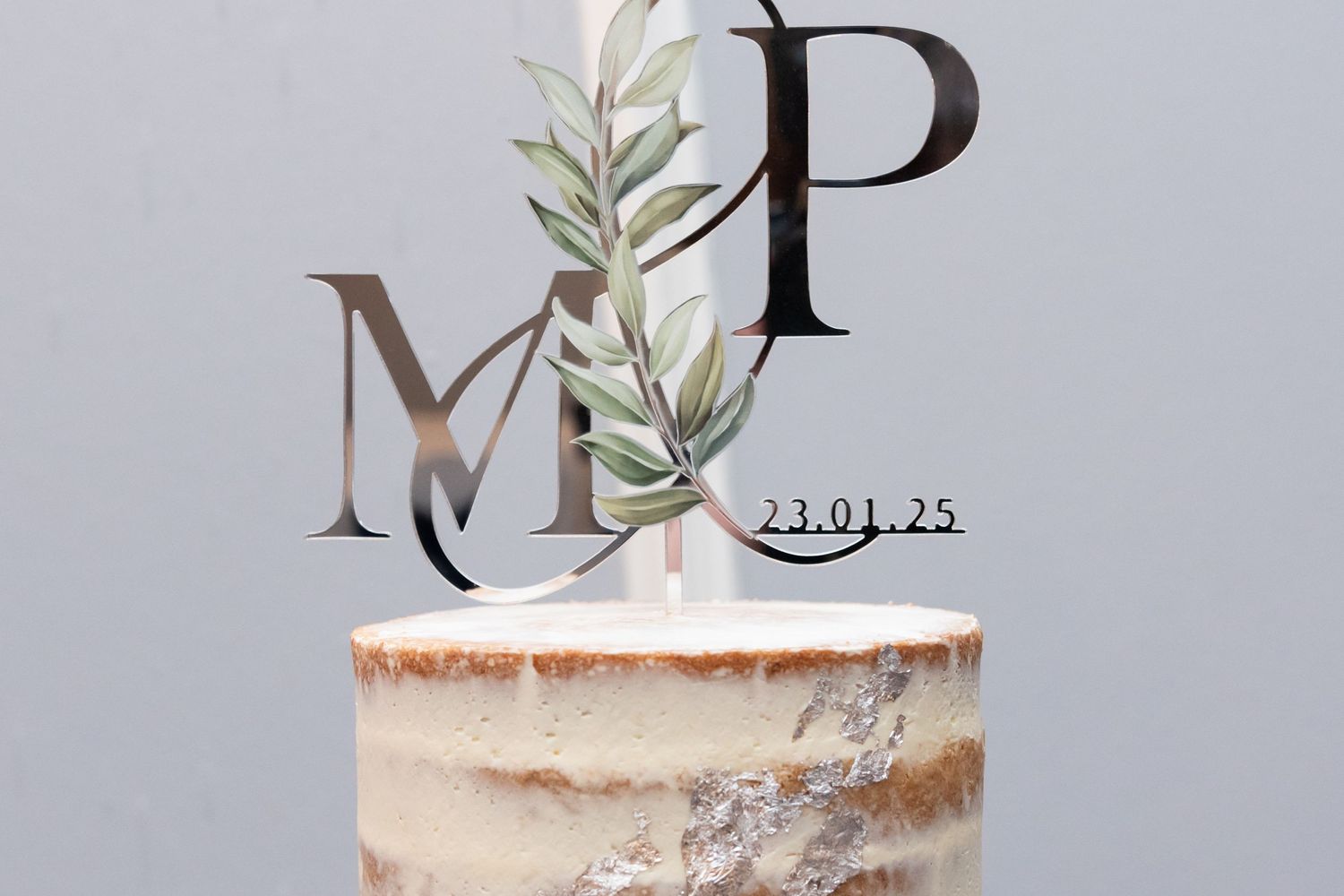 Elegant white cake with metallic letter topper and floral decorations.