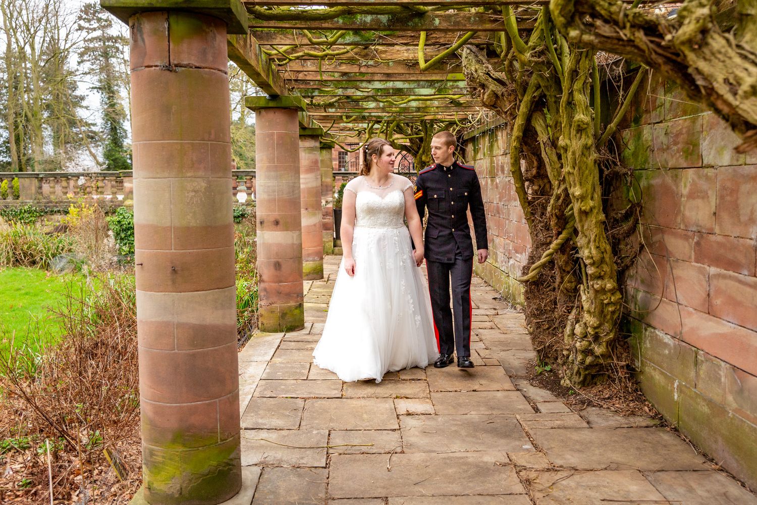 Chester Wedding Photographer - Inglewood Manor Wedding. A bride and groom are walking, holding hands, under a pergola in Autumn.