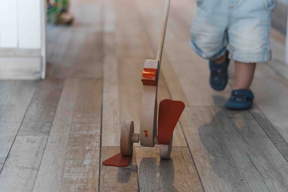 Child pushing a vintage wooden push toy along a hardwood floor.