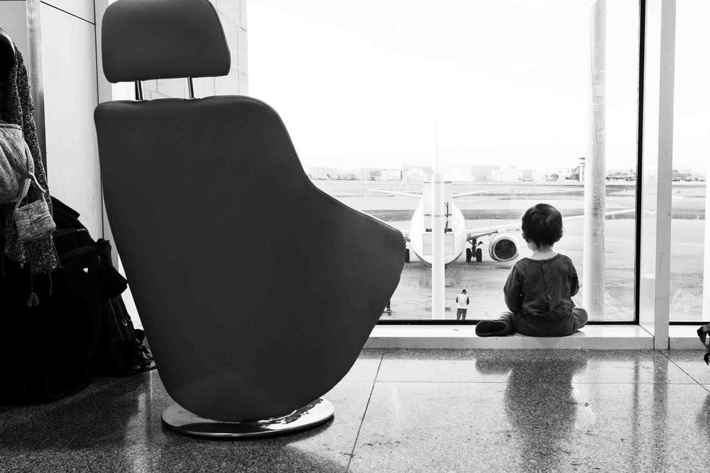 Modern black chair next to large window in airport terminal with view of planes on tarmac.