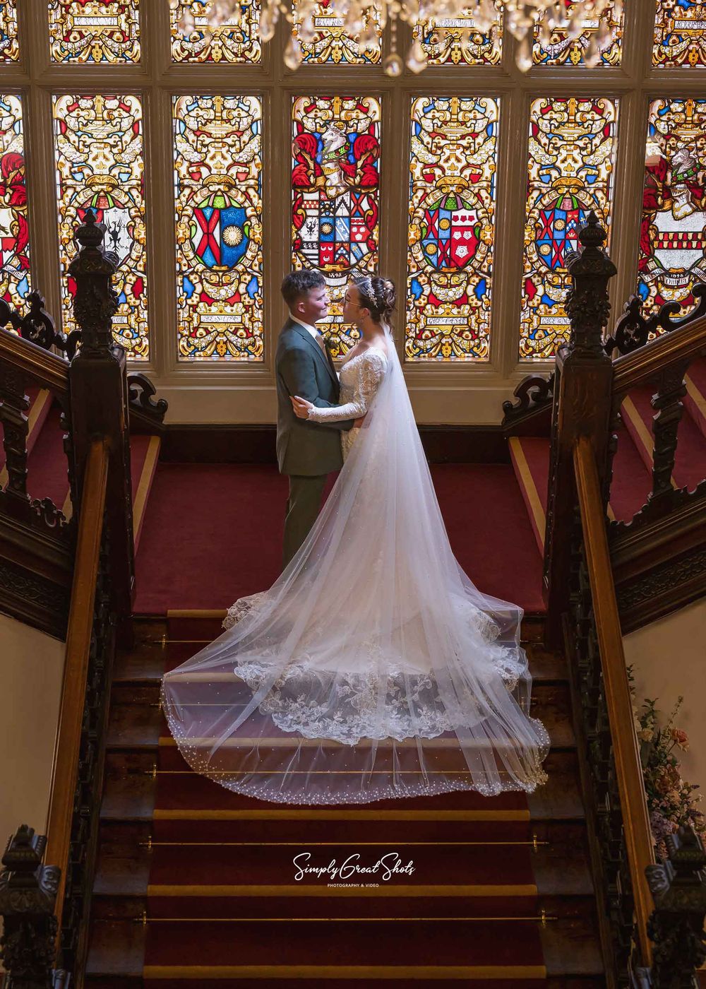 A bride and groom sharing a romantic moment on the grand staircase in front of the historic stained glass windows at Beaumanor Hall in Leice