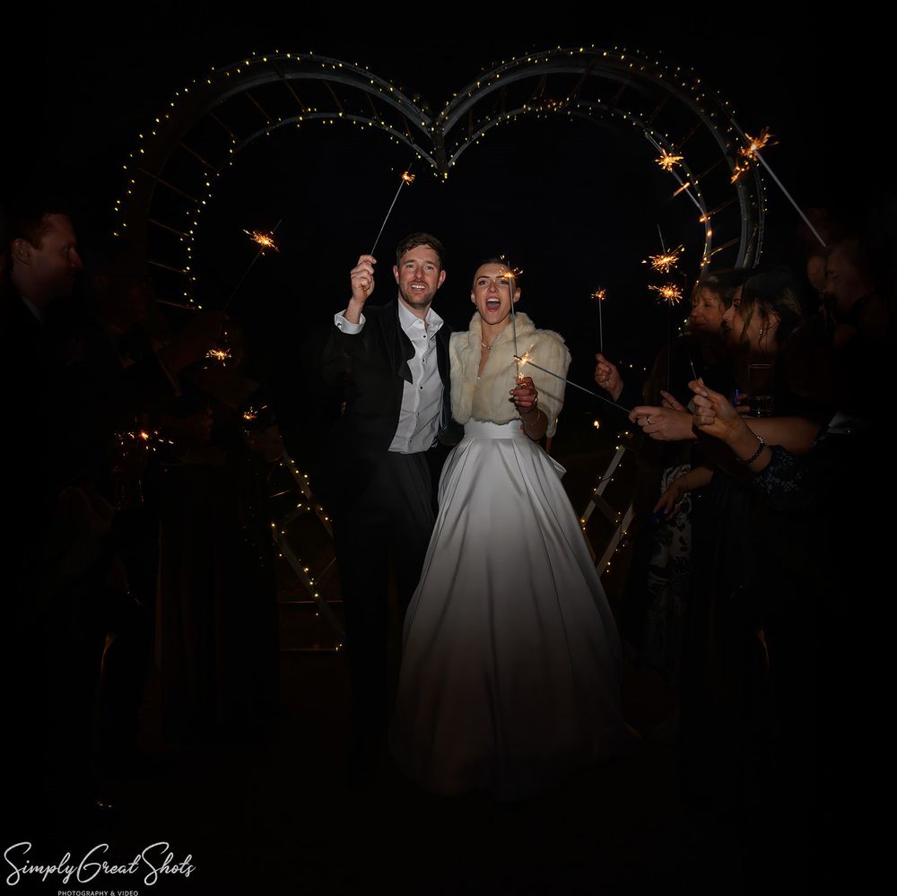 A bride and groom celebrating their wedding with a sparkler send-off in Leicestershire, standing in front of a large heart-shaped light inst