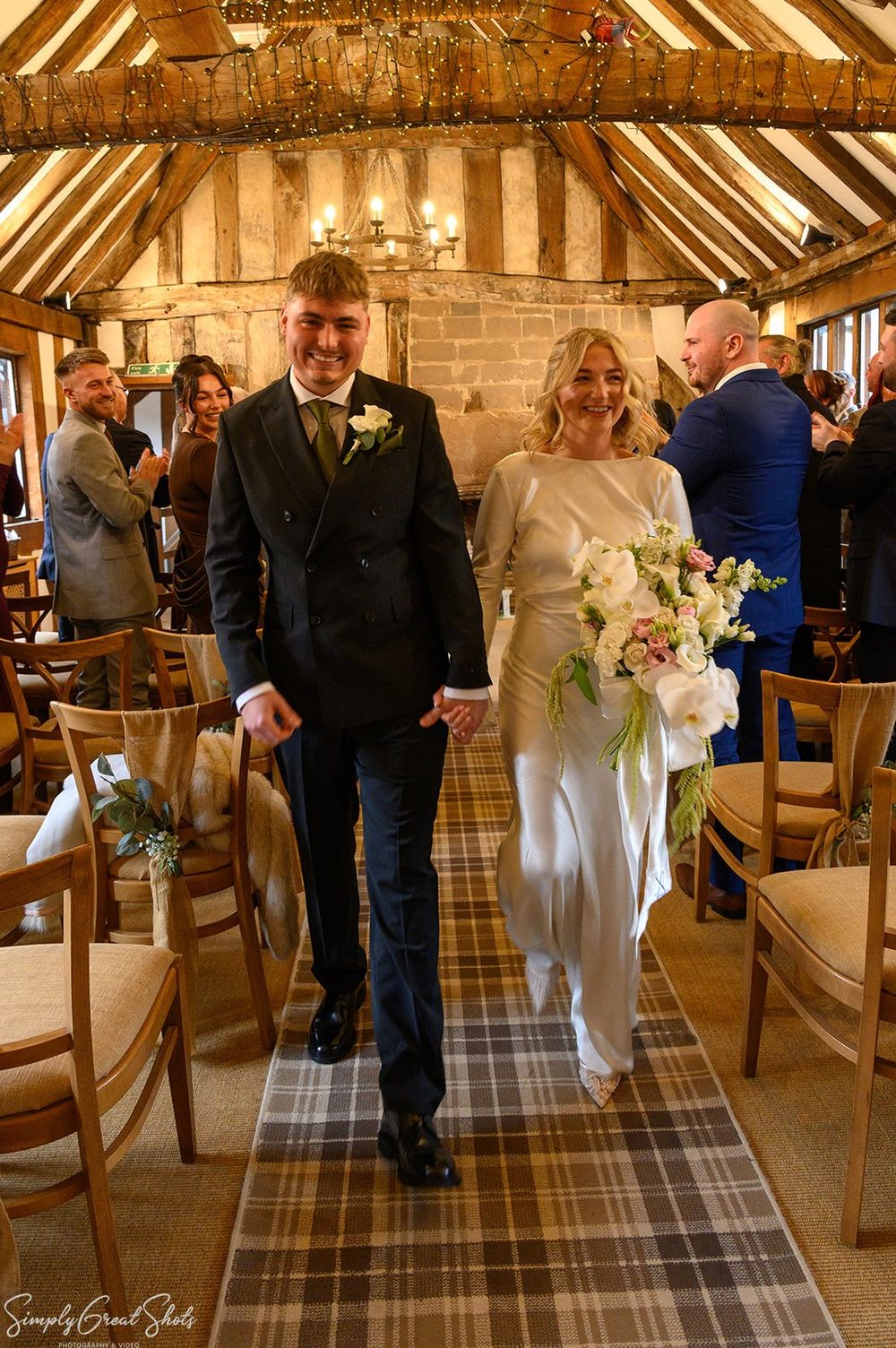 A joyful bride and groom walking hand-in-hand back down the aisle after their wedding ceremony in the rustic timber-beamed room at Cheylesmo